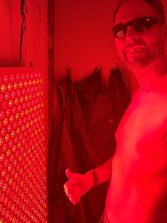 Person står lugnt framför rödljuspanel i Hälsostugan – mjuk återhämtning utan prestation
